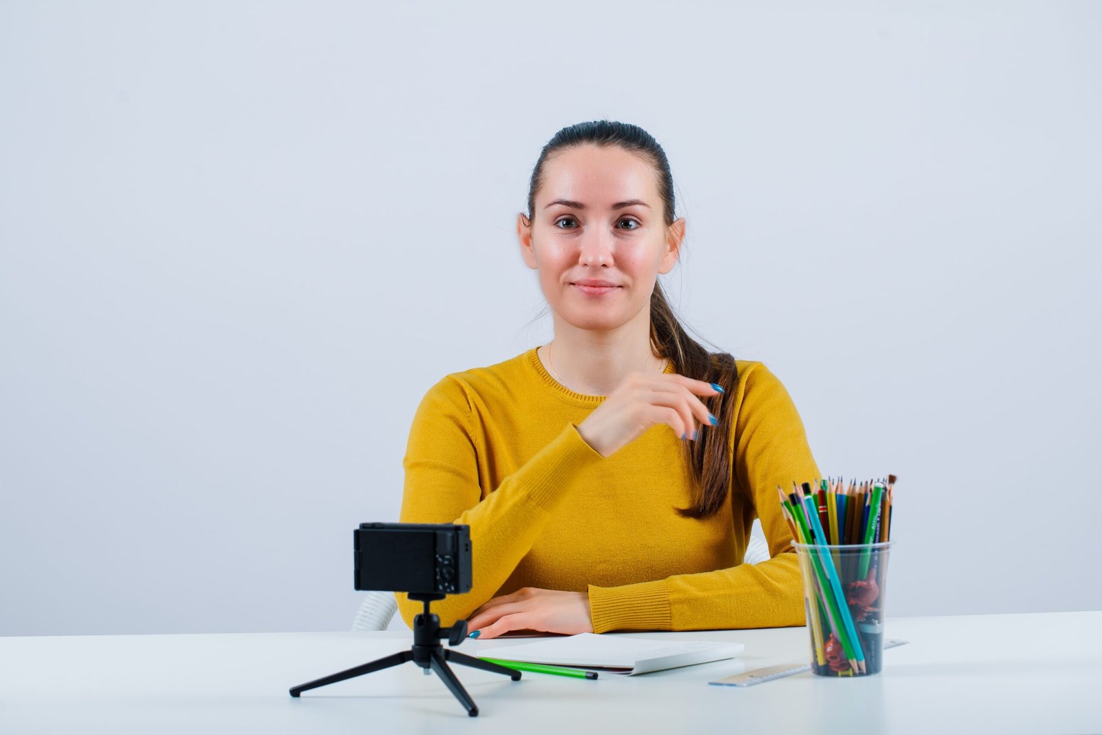 Smiling blogger girl is looking at away by sitting in front of her mini camera on white background